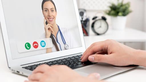 A person is engaged in a conversation on the phone while simultaneously working on a laptop.