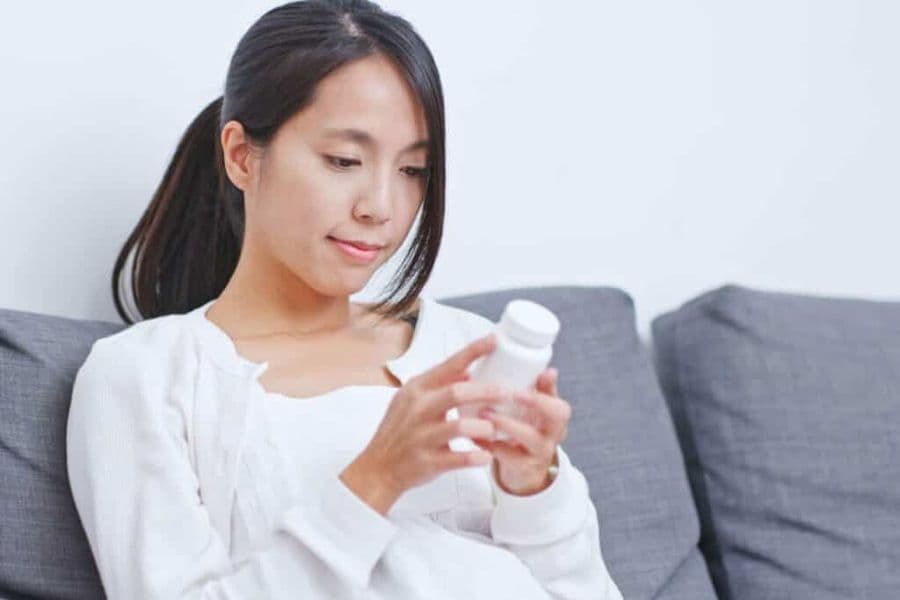 Young woman sitting on a sofa reading a supplement label.