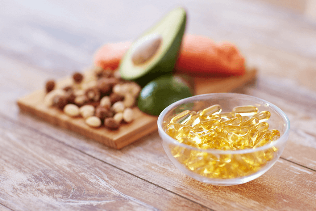 fish oil supplements in a clear bowl next to nuts, avocados, and fish on a board