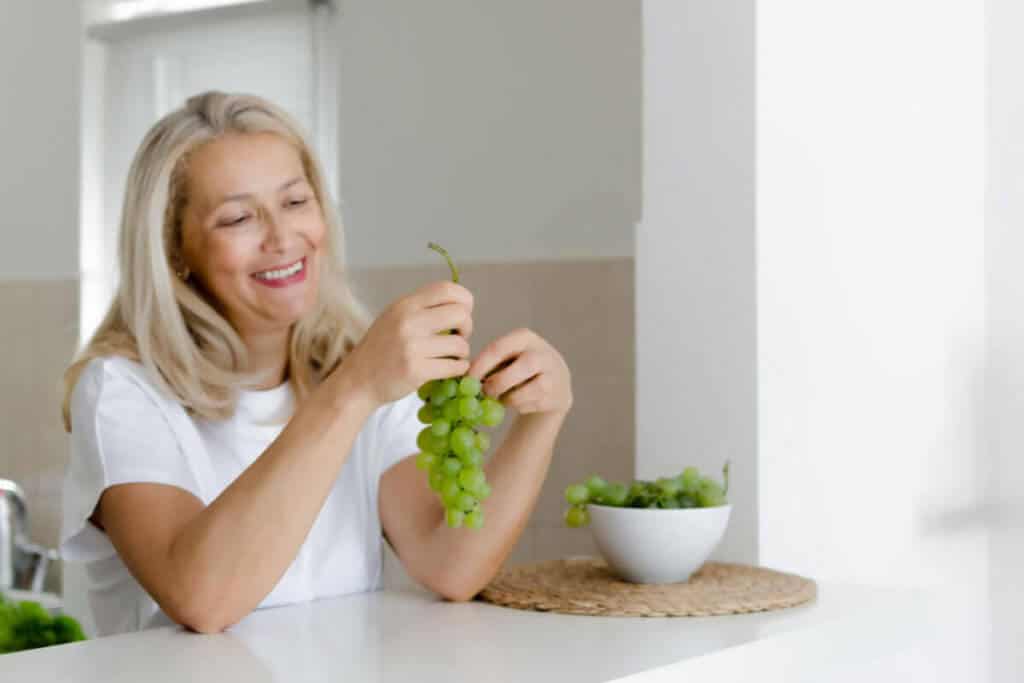 elder woman sitting in kitchen eating grapes