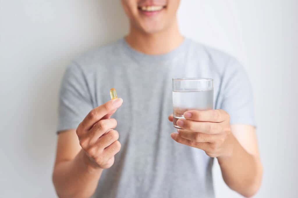 man holding omega 3 supplements in one hand and water in the other