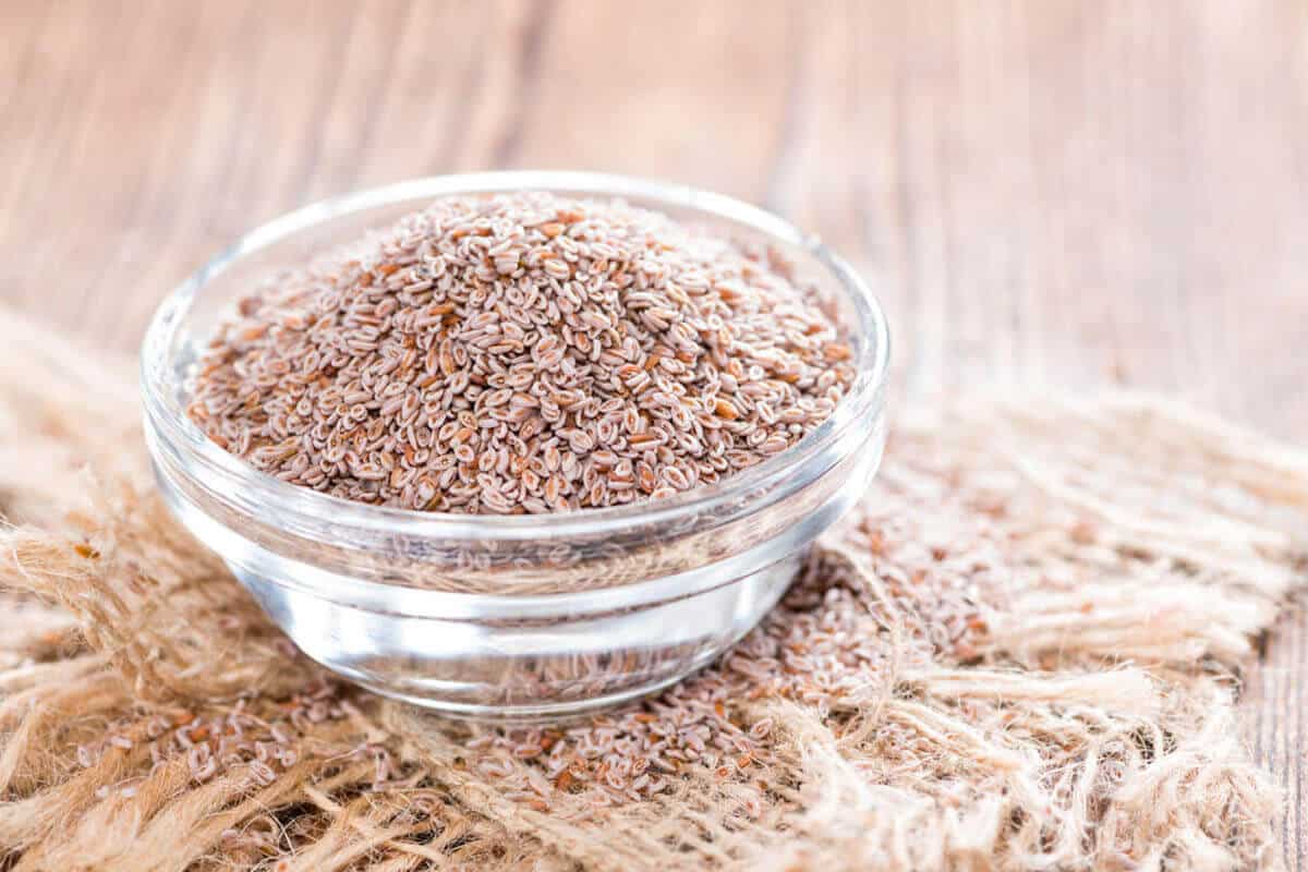 Psyllium seeds in a glass bowl on wooden background.