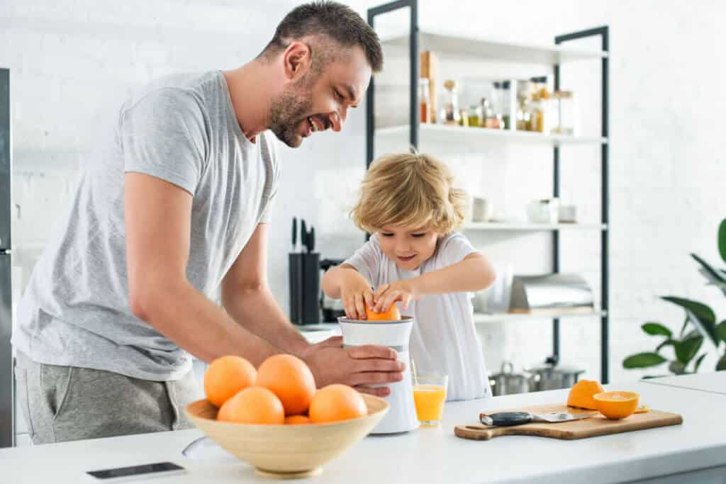 father and daughter making fresh orange juice in kitchen