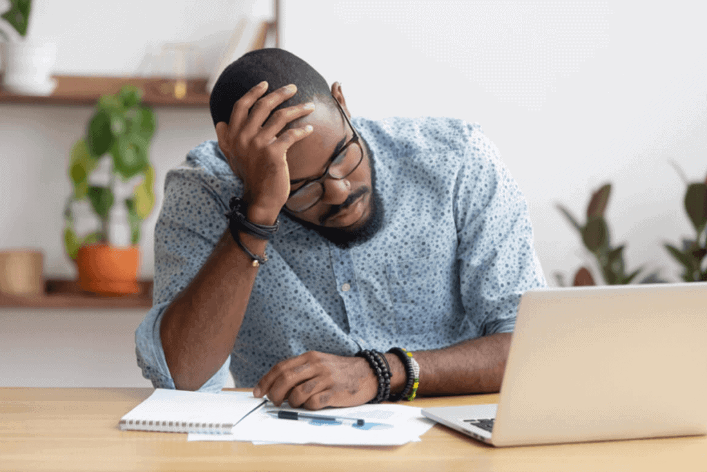 man holding his head looking at computer feeling tired