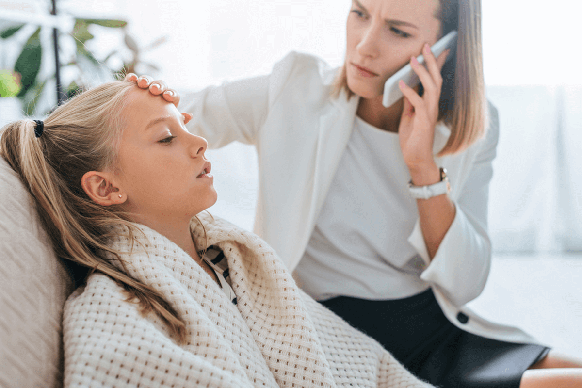 mother feeling daughters forehead for temperature while being on the phone
