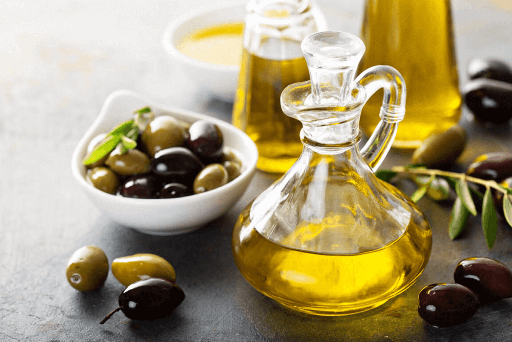Olive oil in glasses and olives in a white dish next to the oil