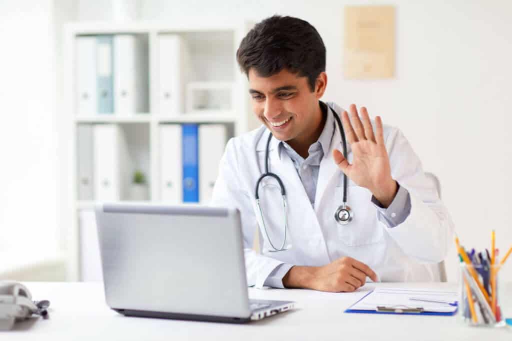 practitioner video calling a patient and waving into their laptop