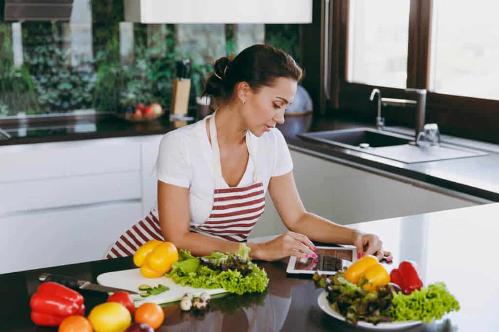 woman with vegetables in kitchen looking at an iPad before cooking