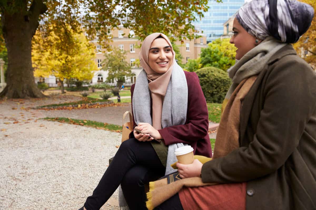 Two women sitting on a bench talking 