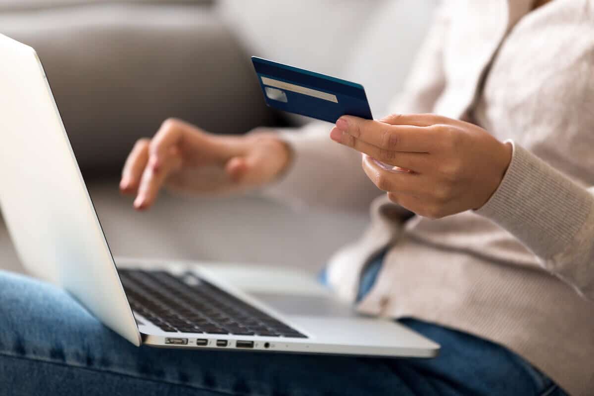close up of person holding card and paying online on laptop