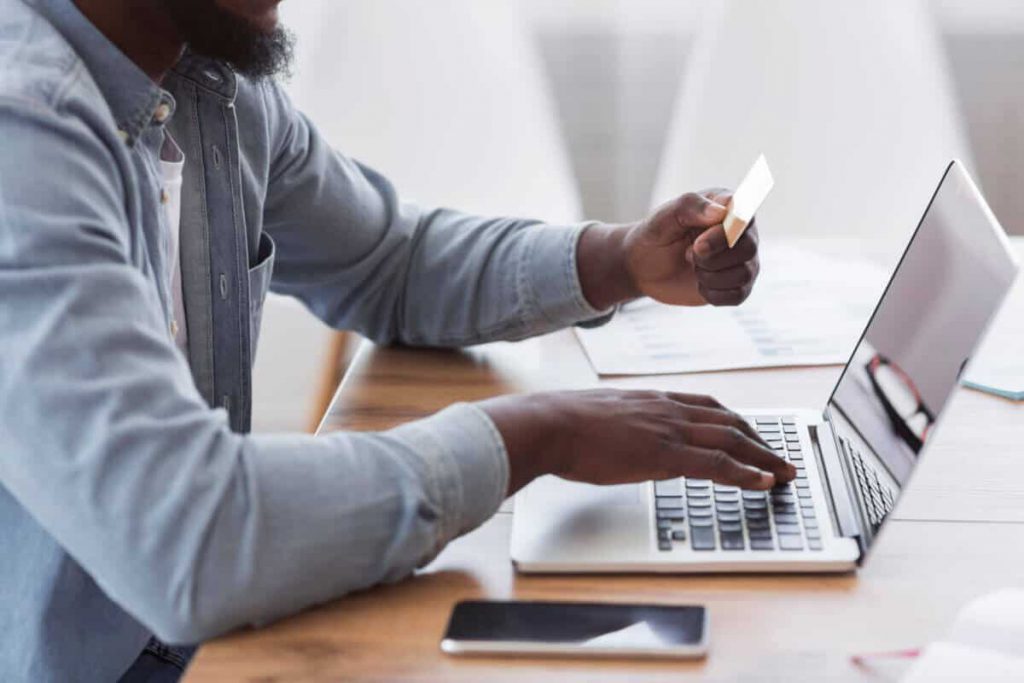 man holding credit card and typing on laptop