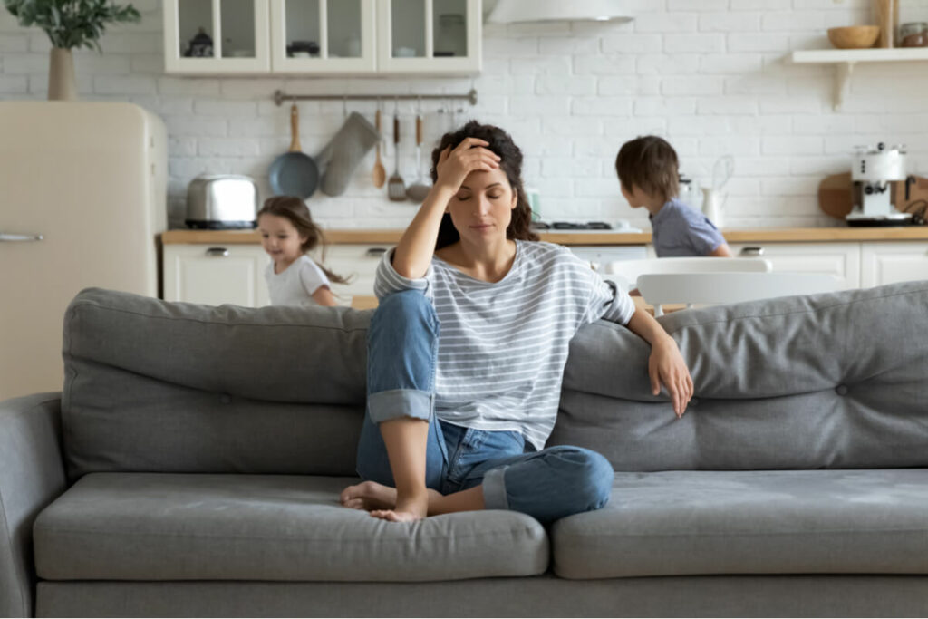 woman stressed on the couch while kids run in the background
