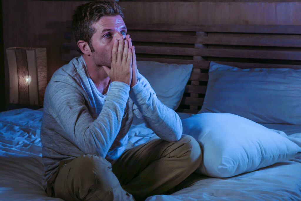 man laying in bed holding his hands over his mouth