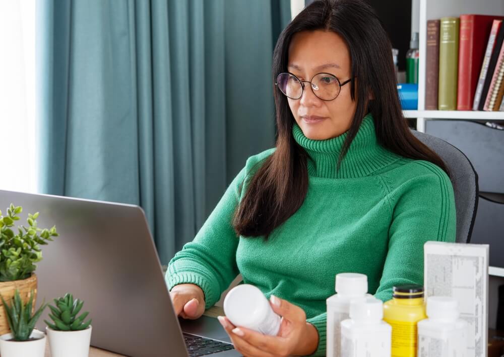 woman holding a supplement bottle using a laptop