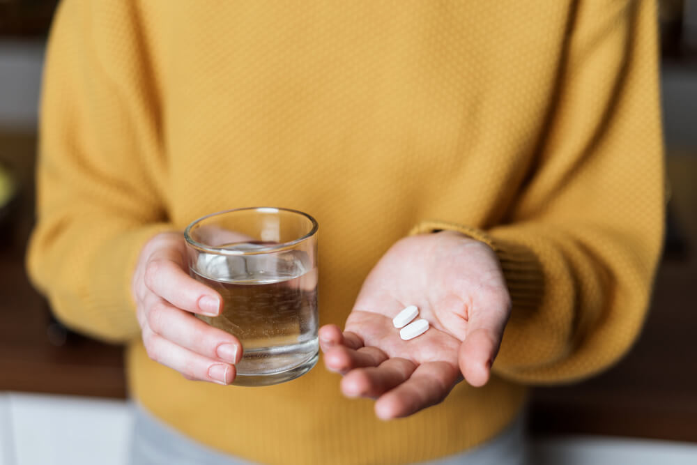 person holding supplements and a glass of water