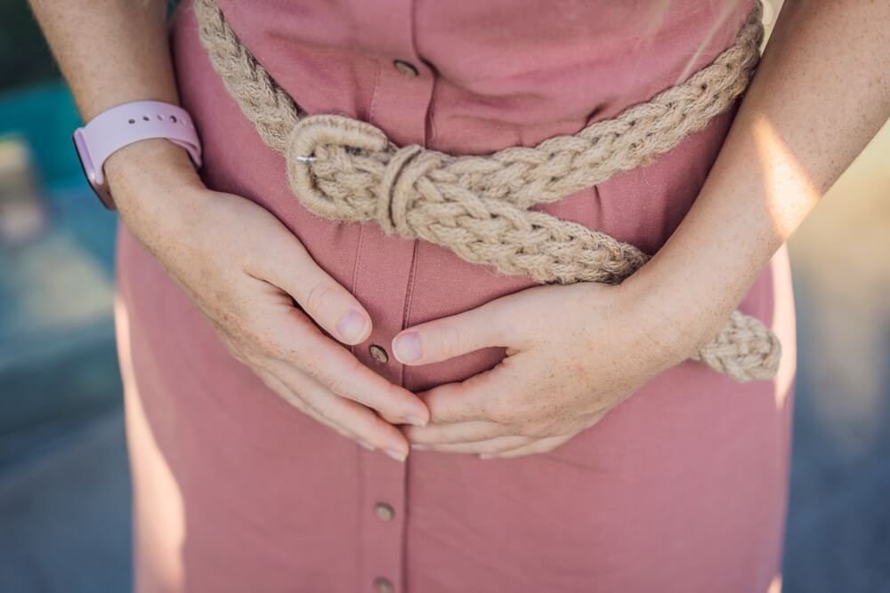 woman wearing pink dress holding abdominal area