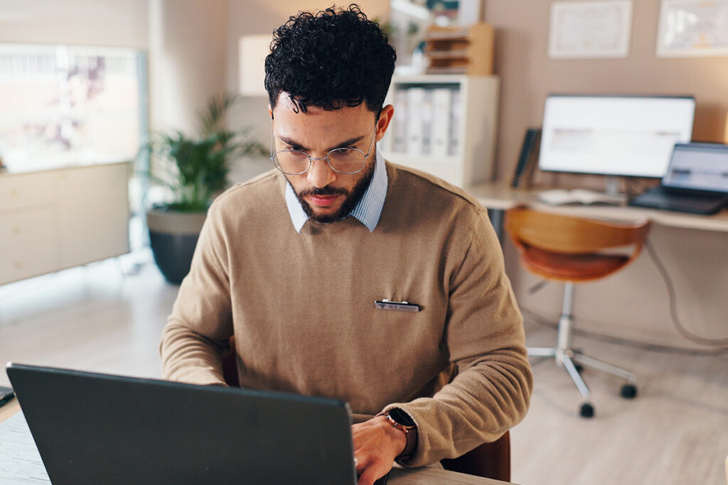 A man is sitting at a desk, focusing on his laptop.