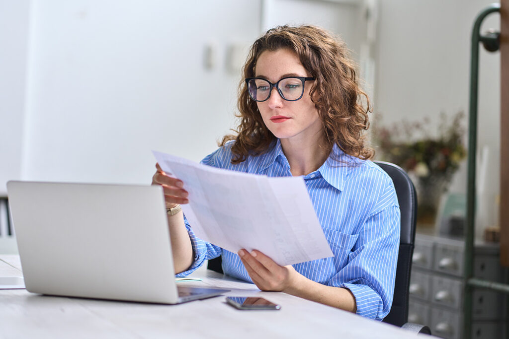 A woman is sitting at a desk reading a paper. She appears focused and engaged in her task.
